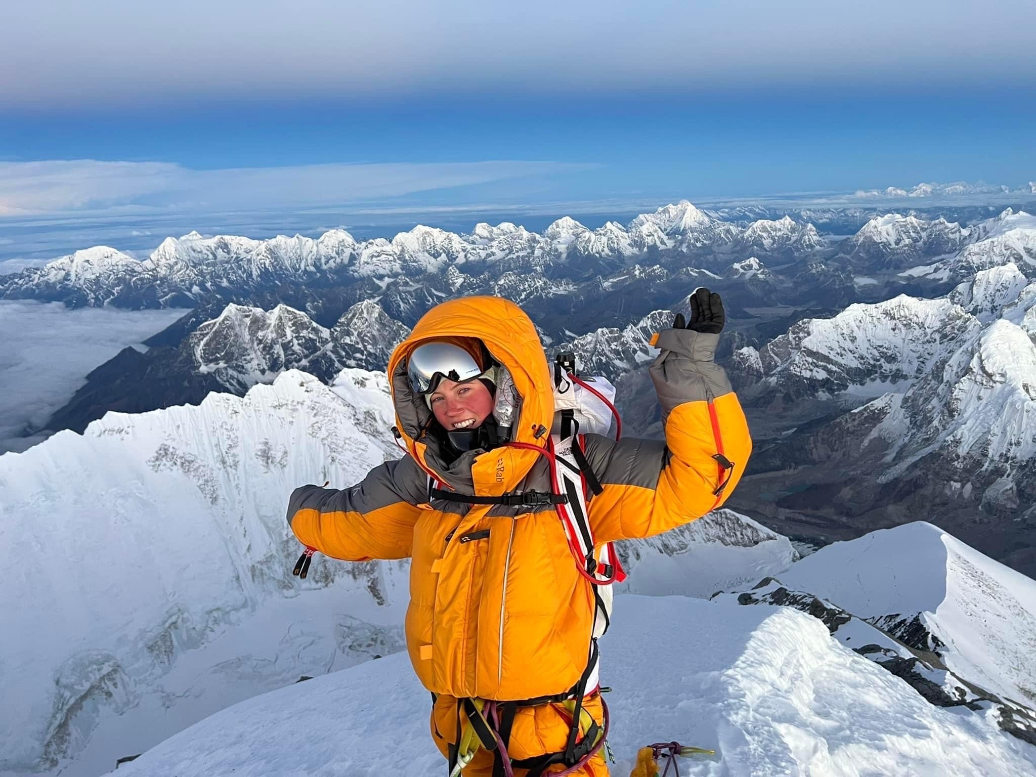 Gabby Kanizay celebrates on the summit of Mount Everest, with rows of snow-capped peaks in the background.